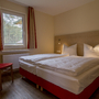 Hotelzimmer mit Doppelbett, Fenster mit Vorhang, Stuhl und Holzboden.