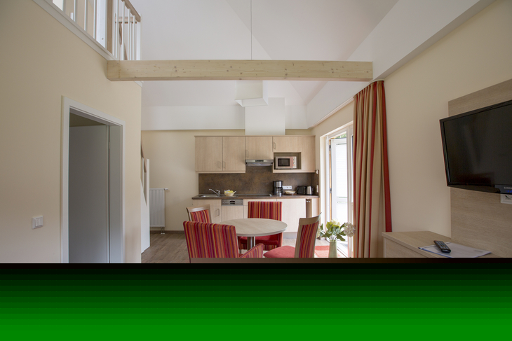 Moderne Ferienwohnung mit Holzbalken, Esstisch und kleiner Küche.