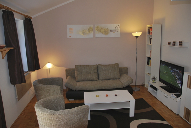 Gemütliches Wohnzimmer mit Sofa, Sessel, Couchtisch und Fernseher.
