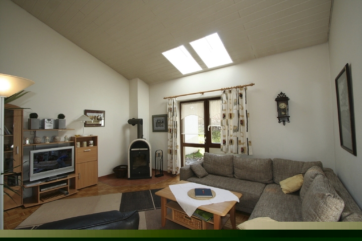 Wohnzimmer mit grauem Ecksofa, Kamin, Fernseher und großem Fenster.