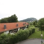 Gebäudekomplex mit roten Dächern und grüner Umgebung, Hügel im Hintergrund.