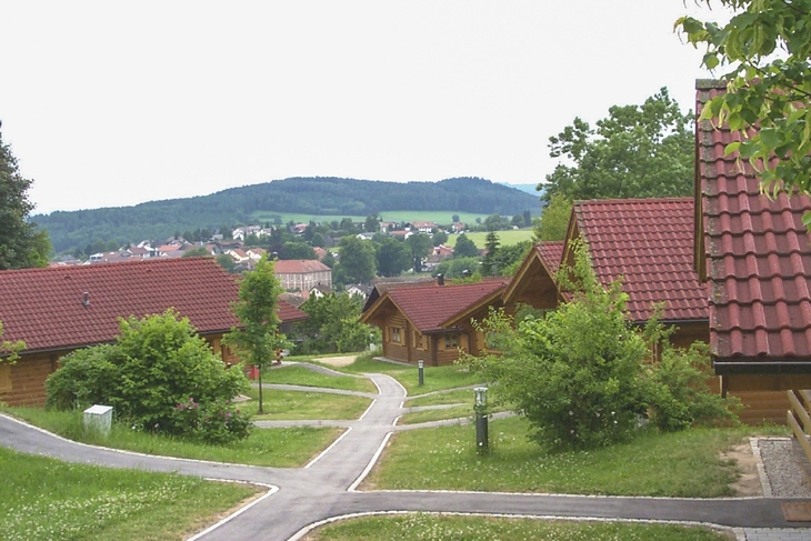 Ferienhäuser in einer grünen Landschaft mit Blick auf Hügel und Ort im Hintergrund.