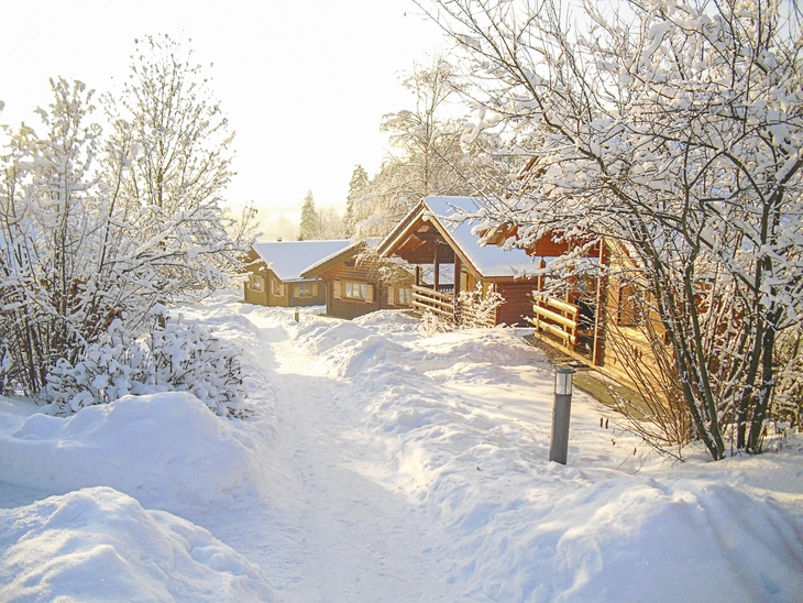 Verschneite Holzhütten in einem Winterwald bei Sonnenschein.