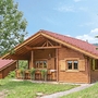 Blockhütte im Naturerlebnisdorf mit Terrasse und Bäumen umgeben.