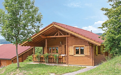Blockhütte im Naturerlebnisdorf mit Terrasse und Bäumen umgeben.