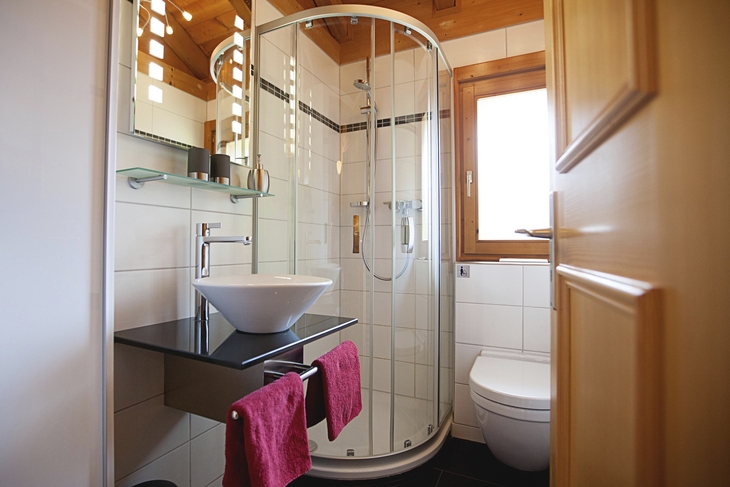 Kleines Badezimmer mit Duschkabine, weißer Keramik und Holzdetails.
