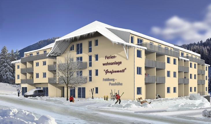 Mehrstöckige Ferienwohnanlage im Schnee mit Skifahrern davor.