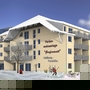 Mehrstöckige Ferienwohnanlage im Schnee mit Skifahrern davor.