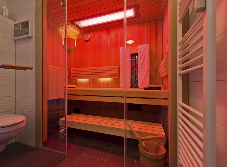Innenansicht einer Sauna mit Holzbänken und roten Infrarotlichtern.