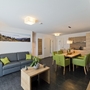 Modernes Wohnzimmer mit grauem Sofa, Esstisch und grünen Stühlen.