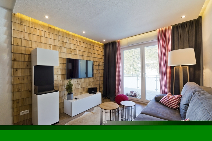 Modernes Wohnzimmer mit grauem Sofa, TV, Holzverkleidung und Fenstertüren.