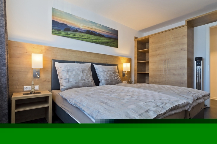 Hotelzimmer mit Doppelbett, Holzdekor, Lampen und Landschaftsbild an der Wand