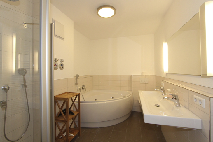 Badezimmer mit Dusche, Badewanne, Waschbecken, Spiegel und Holzregal.
