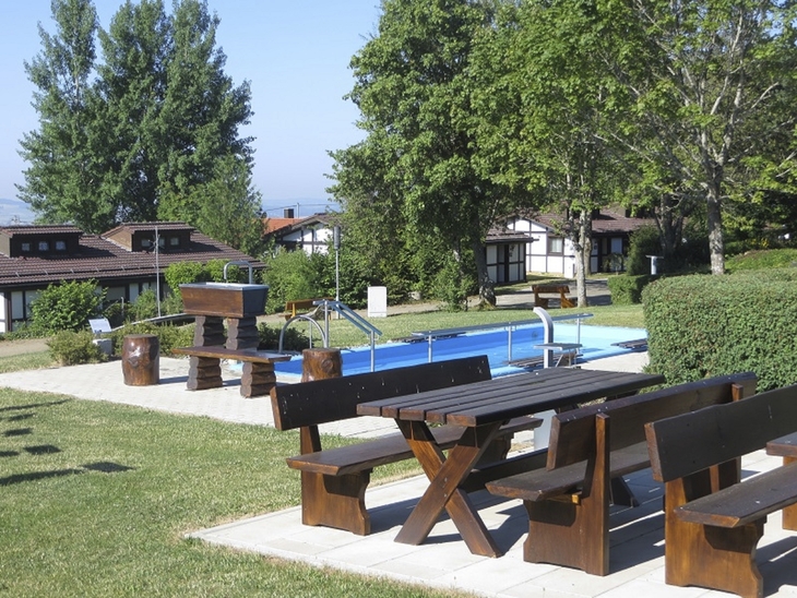 Gartenbereich mit Holzbänken und kleinem Pool im Feriendorf bei Sonnenschein.