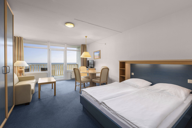 Helles Hotelzimmer mit Doppelbett, Sofa, Tisch und Meerblick auf Fehmarn.
