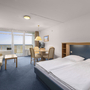 Helles Hotelzimmer mit Doppelbett, Sofa, Tisch und Meerblick auf Fehmarn.