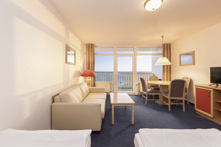 Ein gemütliches Hotelzimmer mit Sofa, Tisch und Blick auf das Meer.