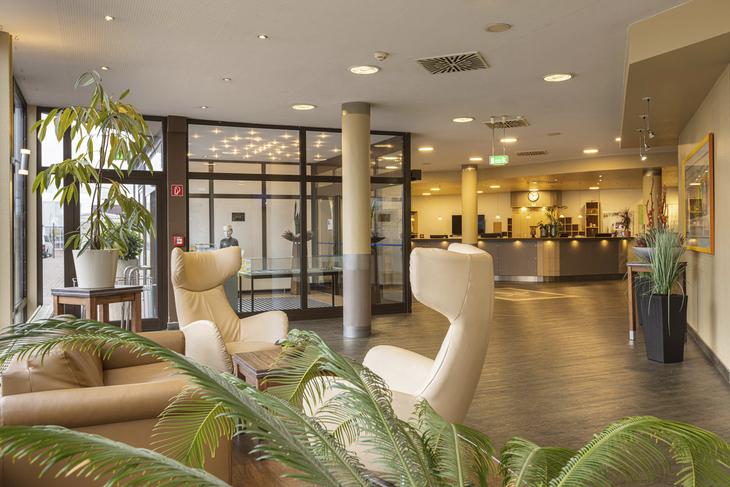 Hotel-Lobby mit Sitzbereich, Pflanzen und Rezeption im Hintergrund.