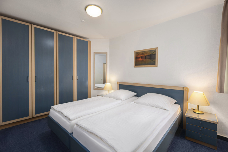 Schlafzimmer mit Doppelbett, blauen Schränken und Nachttischlampen.