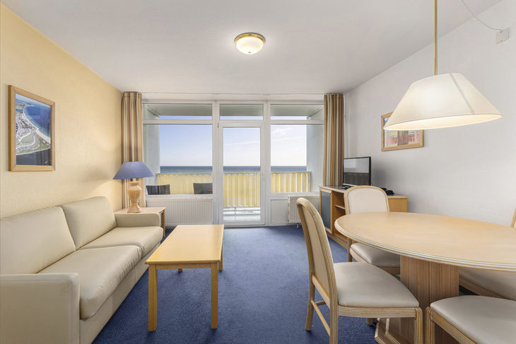Wohnzimmer einer Ferienwohnung mit Sofa und Essbereich, Zugang zum Balkon mit Meerblick.