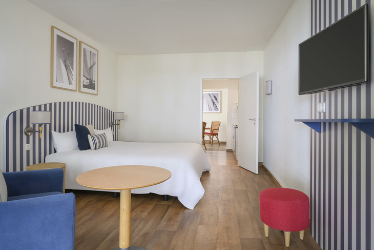 Hotelzimmer mit Doppelbett, blau-weiß gestreifter Tapete, Tisch, Stühlen und Fernseher.