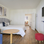 Hotelzimmer mit Doppelbett, blau-weiß gestreifter Tapete, Tisch, Stühlen und Fernseher.