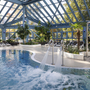 Innenbereich eines Pools mit Glasdach und Liegestühlen im Hintergrund.
