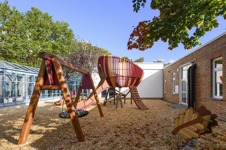 Spielplatz mit Klettergerüst und Schaukel im Freien bei Sonnenschein.