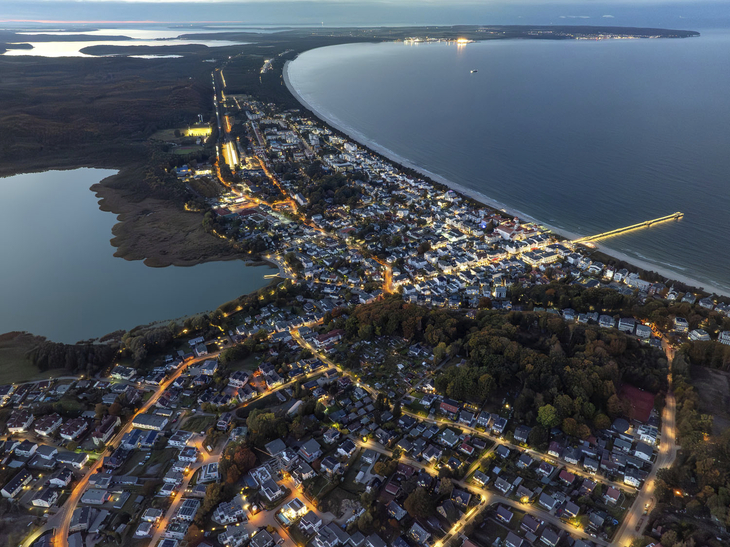 Luftaufnahme von Binz auf Rügen bei Abenddämmerung, Küstenlinie und beleuchtete Straßen.