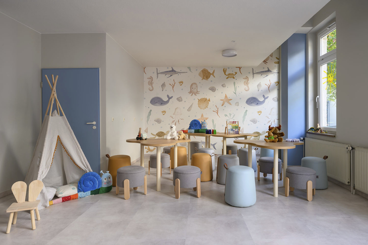 Kinderclubraum mit Spielzeug, Tischen und bunten Hockern.
