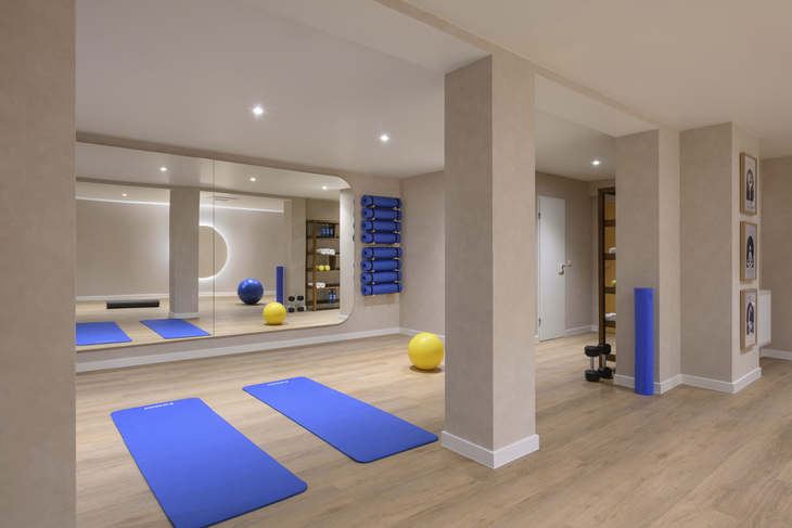 Moderner Fitnessraum mit blauen Matten, Fitnessbällen und Spiegelwand.