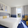 Helles Hotelzimmer mit Doppelbett, blauer Teppich und Balkon in Binz, Rügen.