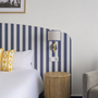 Hotelzimmer mit gestreiftem Kopfteil, gelben Kissen und Tischlampe.