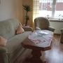 Wohnzimmer mit grauem Sofa, zwei Sesseln, Tisch und großem Fenster.