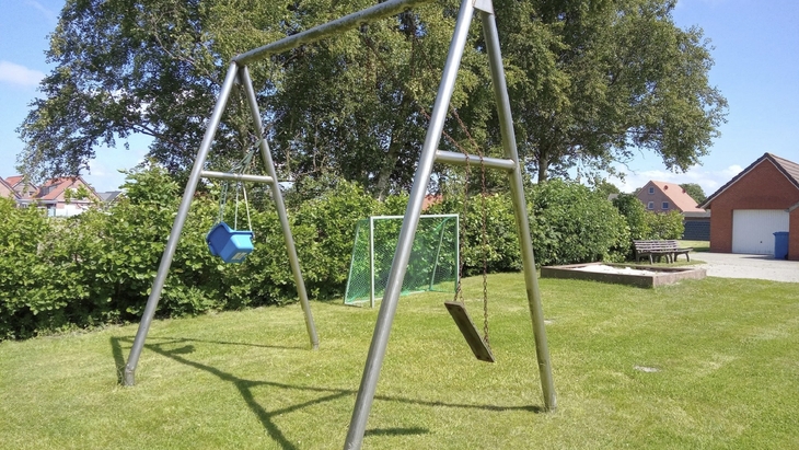 Garten mit Spielplatz, Schaukeln und Bäumen unter blauem Himmel.
