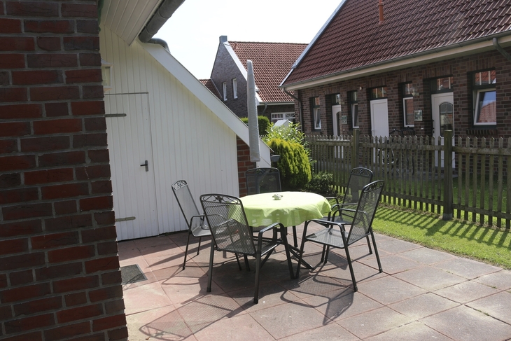 Garten mit Tisch und Stühlen auf einer gepflasterten Terrasse, umgeben von Backsteinbauten.