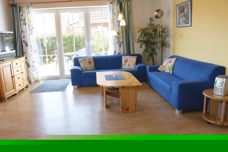 Wohnzimmer mit blauen Sofas, Holztisch und großen Fenstern mit Blick nach draußen.