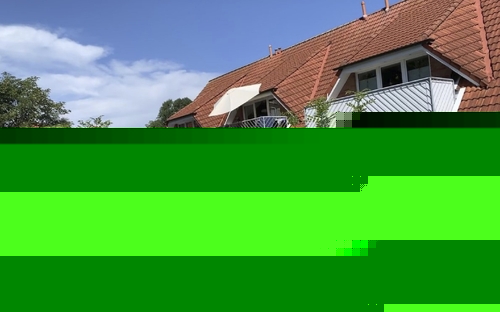 Backstein-Reihenhäuser mit roten Dächern und kleinen Balkonen im Sonnenschein.