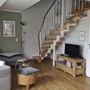 Wohnzimmer mit Sofa, Sessel, Fernseher und offener Treppe auf Holzboden.