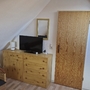 Dachzimmer mit Holzkommode, Fernseher und Tür, neben Rattanstuhl unter Dachschräge.