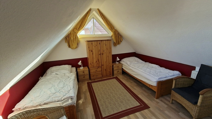 Dachzimmer mit zwei Einzelbetten, gelben Vorhängen und Holzmöbeln.