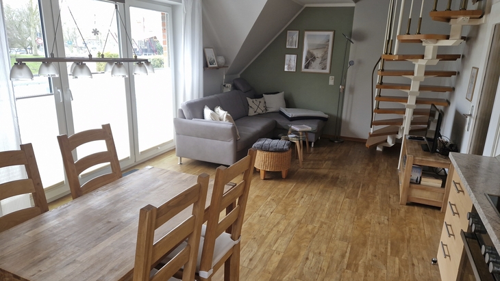 Wohnzimmer mit Holzboden, Treppe, Sofa, Esstisch und großen Fenstern.