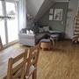 Wohnzimmer mit Holzboden, Treppe, Sofa, Esstisch und großen Fenstern.