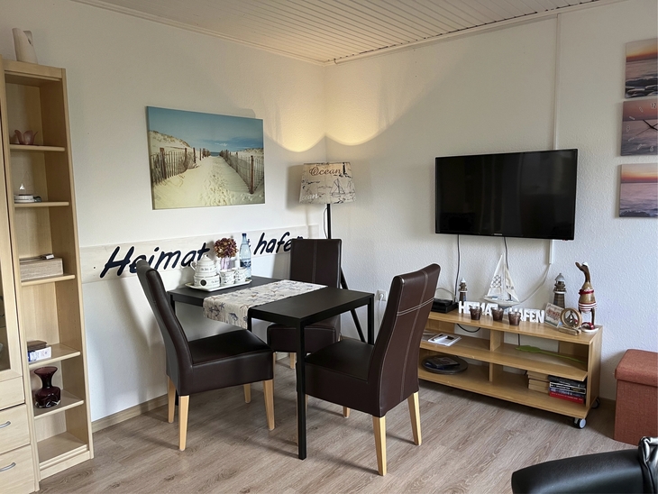 Essbereich in einer Ferienwohnung mit Tisch, Stühlen und TV an der Wand.
