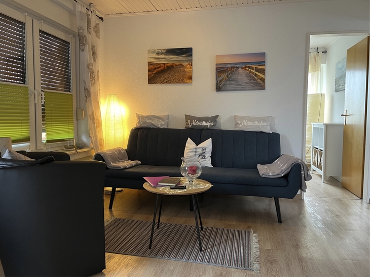 Wohnzimmer mit Sofa, Sessel, Wandbildern und Lampe in einer Ferienwohnung.