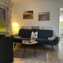 Wohnzimmer mit Sofa, Sessel, Wandbildern und Lampe in einer Ferienwohnung.