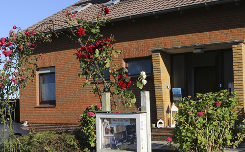 Außenansicht eines Backsteinhauses mit blühenden Rosen im Vordergrund.