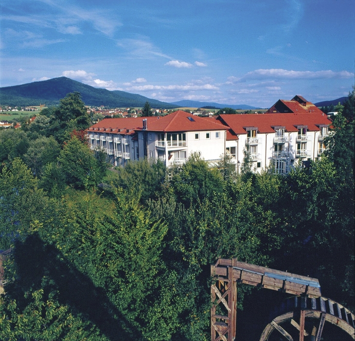 Hotelgebäude mit roten Dächern in grüner Landschaft, Berg im Hintergrund.