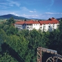 Hotelgebäude mit roten Dächern in grüner Landschaft, Berg im Hintergrund.