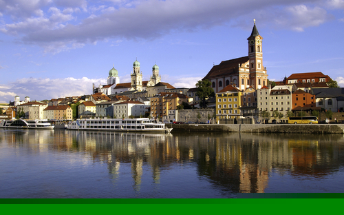 Außenansicht eines Hotels am Flussufer mit Stadt im Hintergrund.